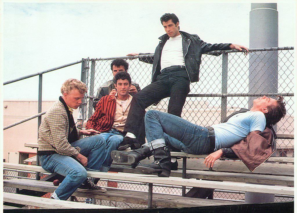 John Travolta hanging out with his crew on the bleachers in a scene from the film ‘Grease’, 1978.