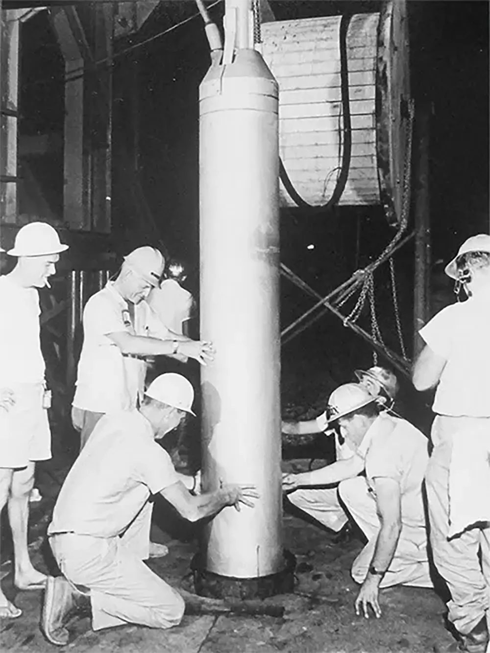 #11 Workers lower the 5.3-kiloton bomb used in the Salmon test into the ground.