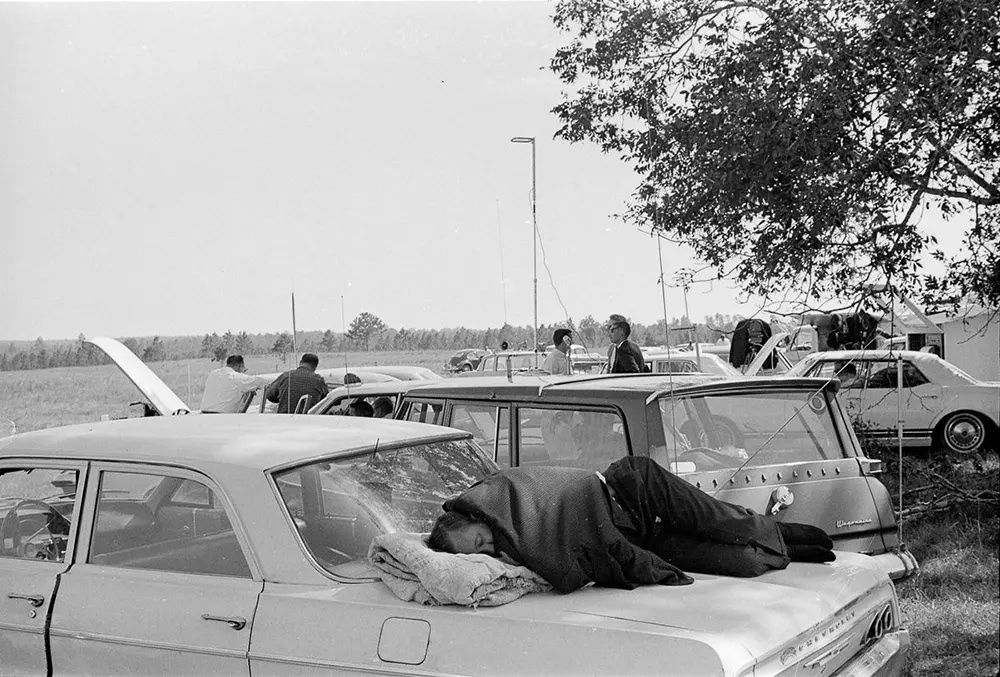 #2 A reporter naps on his car at the media observation point during a postponement.