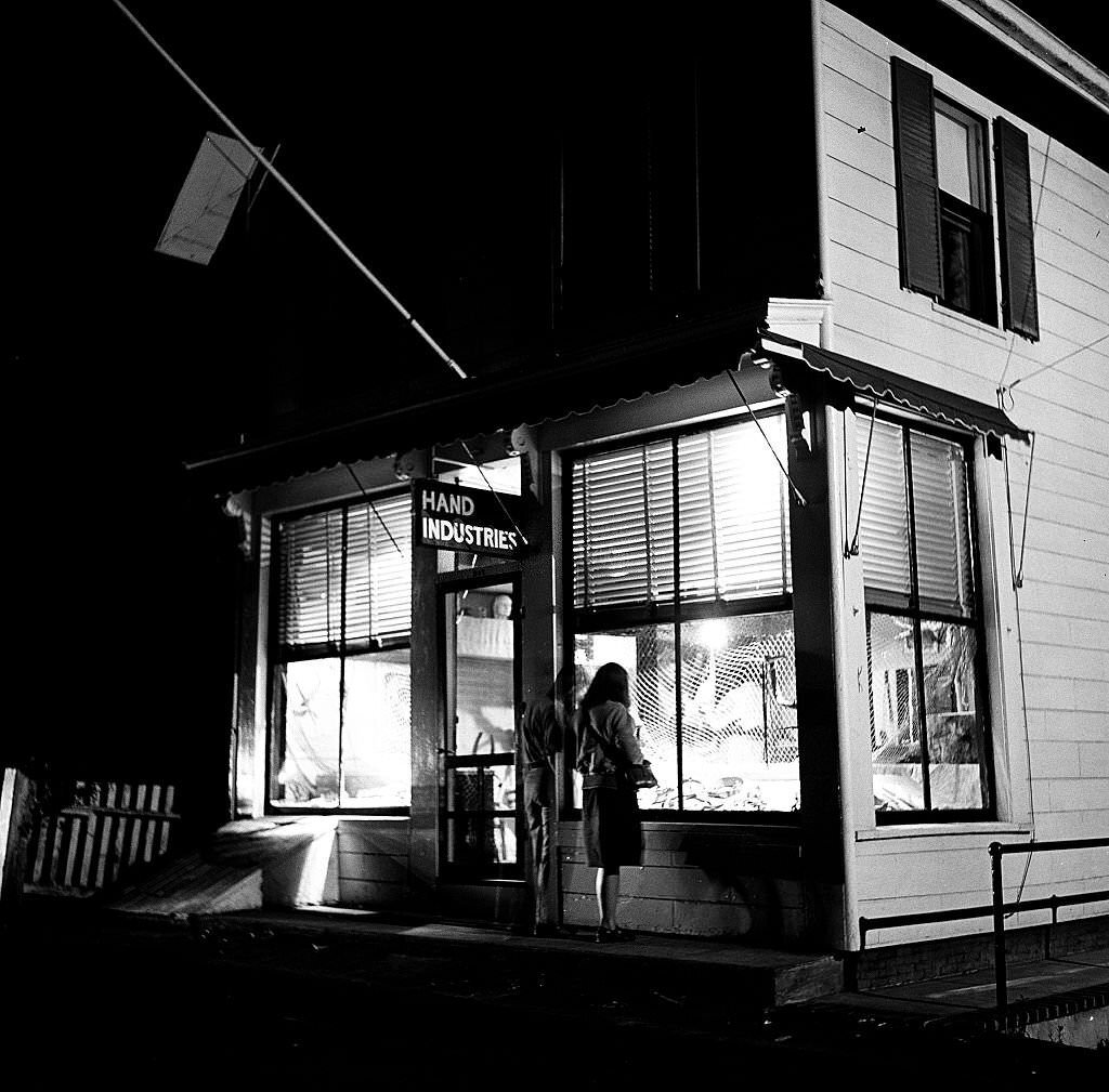#107 Night time view as two visitors look intot the window of the Hand Industries shop, Provincetown, Massachusetts, 1948.