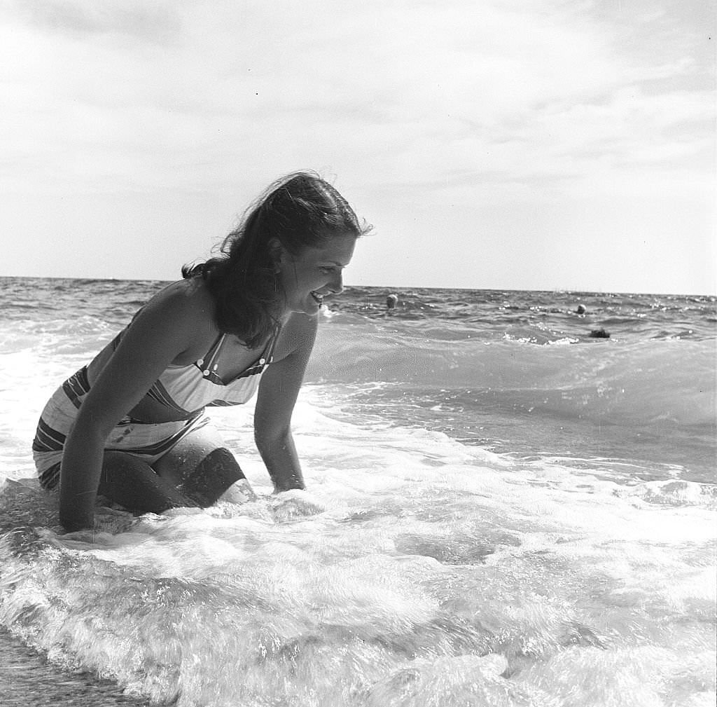 #125 A woman smiles while sitting on the beach as the surf rolls, Provincetown, Massachusetts, 1948.