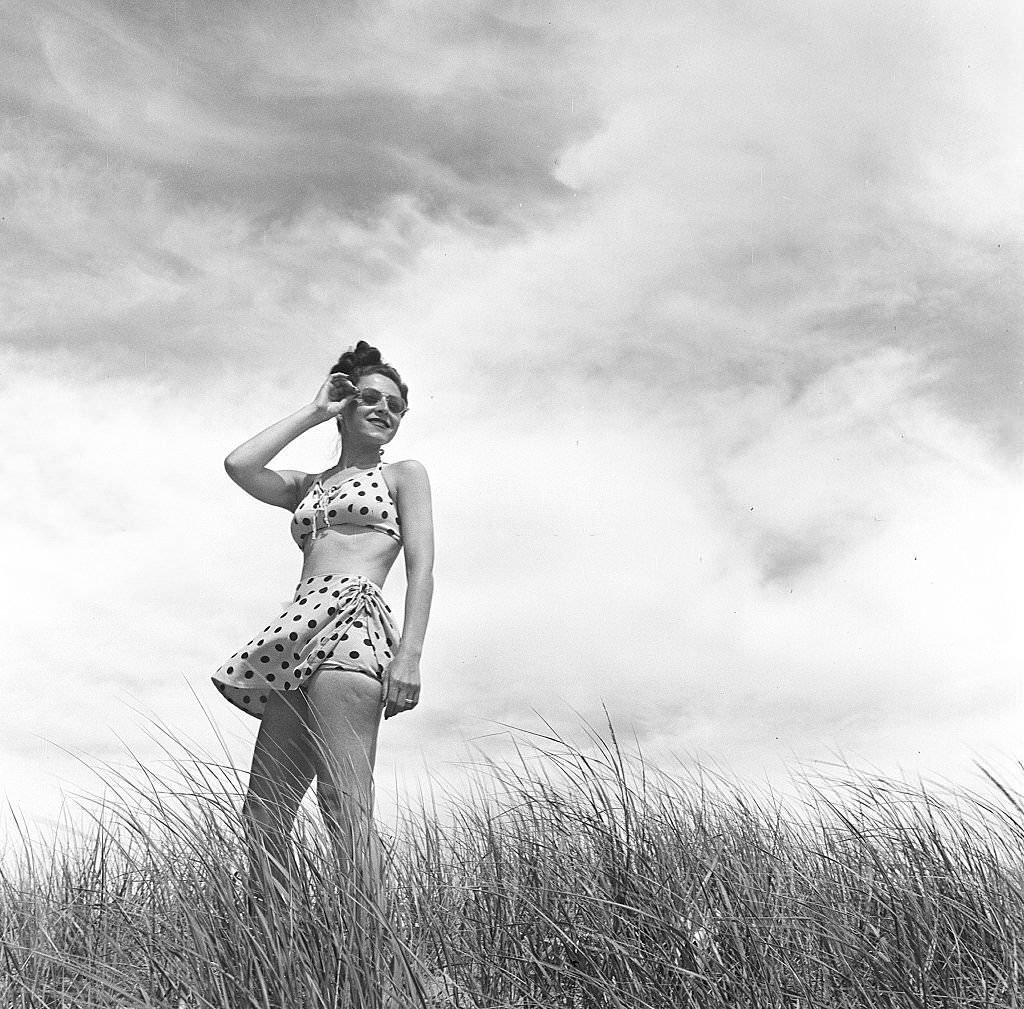 #128 A woman wearing a polka dot bathing suit and standing among the plants on the beach, Provincetown, Massachusetts, 1948.