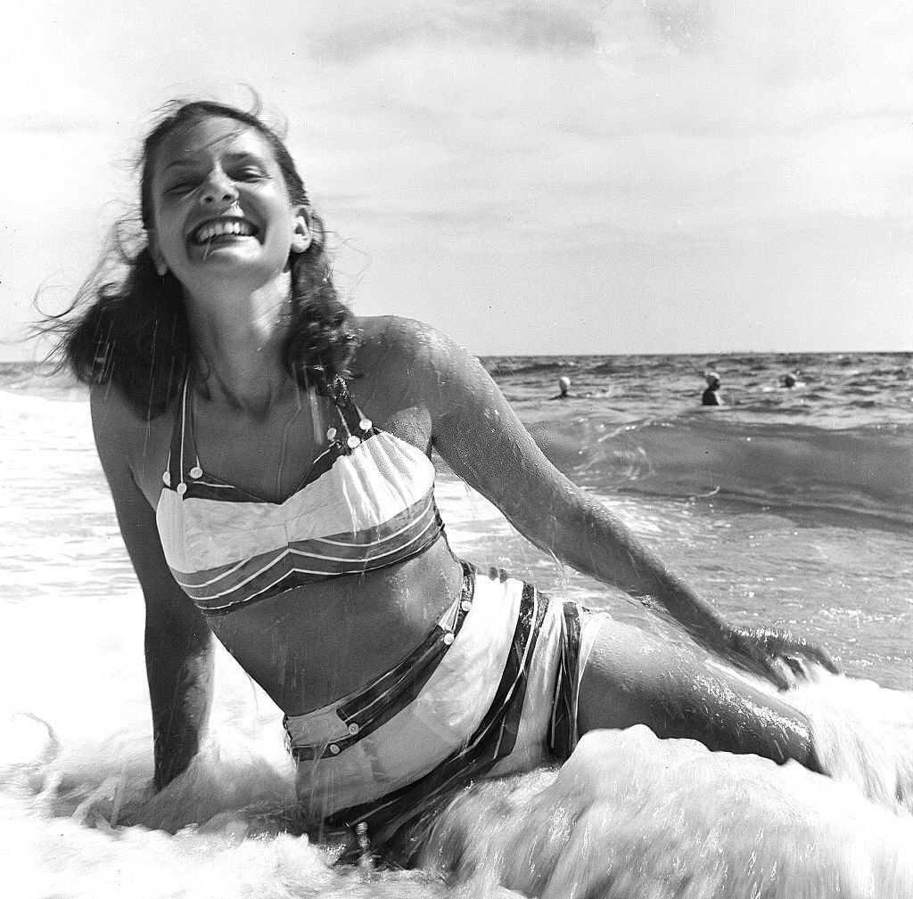 #136 A woman smiles while sitting on the beach as the surf rolls, Provincetown, Massachusetts, 1948.