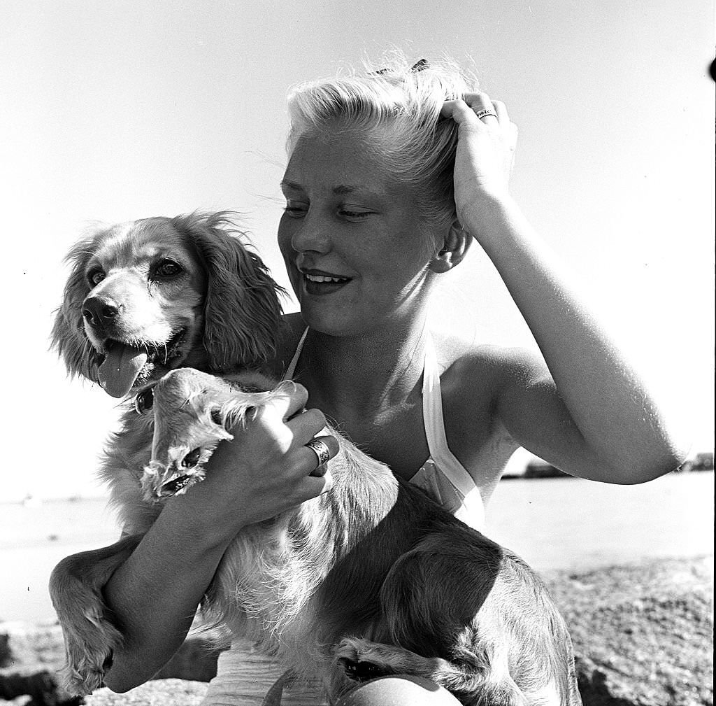 #139 A woman runs her hand through her hair while sitting with her dog, on the beach, Provincetown, Massachusetts, 1948.