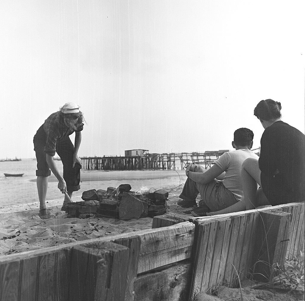 #142 A man and a woman sit while another woman tends the fire for their beachside cookout, Provincetown, Massachusetts, 1948.