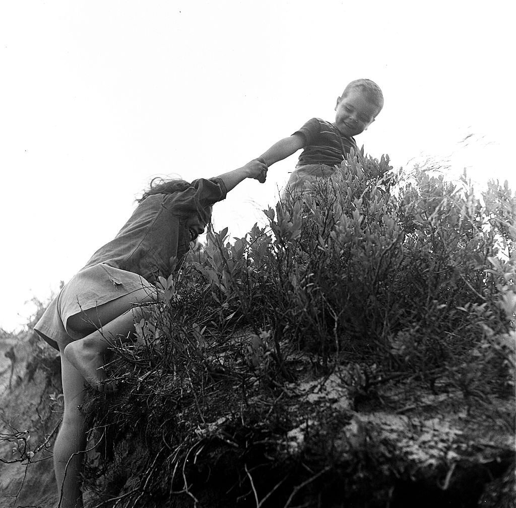 #147 A young boy holds a girl’s hand as he helps her up the sand dunes of the beach, Provincetown, Massachusetts, 1948.
