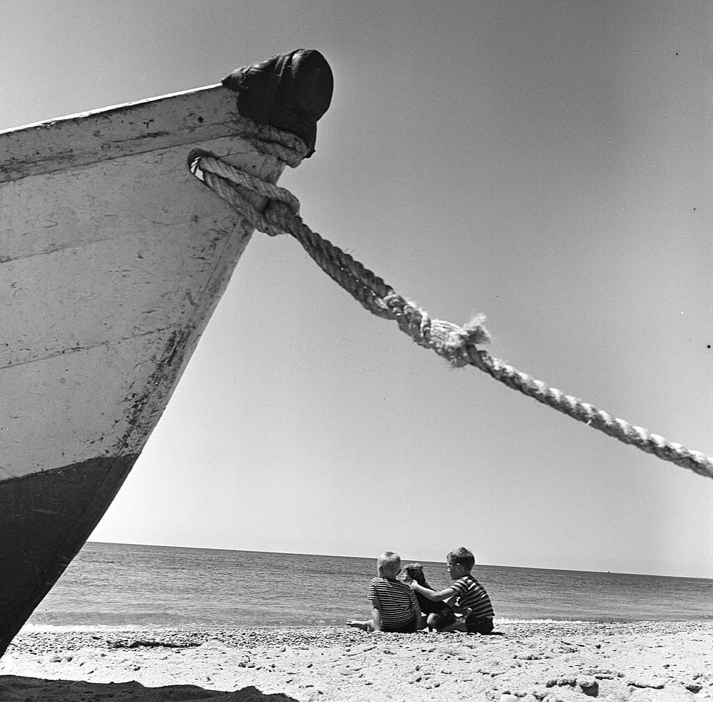 #7 Two young boys sit on the beach with their dog, with a rowboat anchored in the foreground on Cape Cod, Provincetown, Massachussetts, 1947.