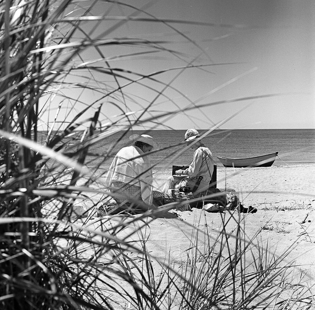#70 A man and a woman, partially obscured by brush, have a picnic on the beach on Cape Cod, Provincetown, Massachussetts, 1947.