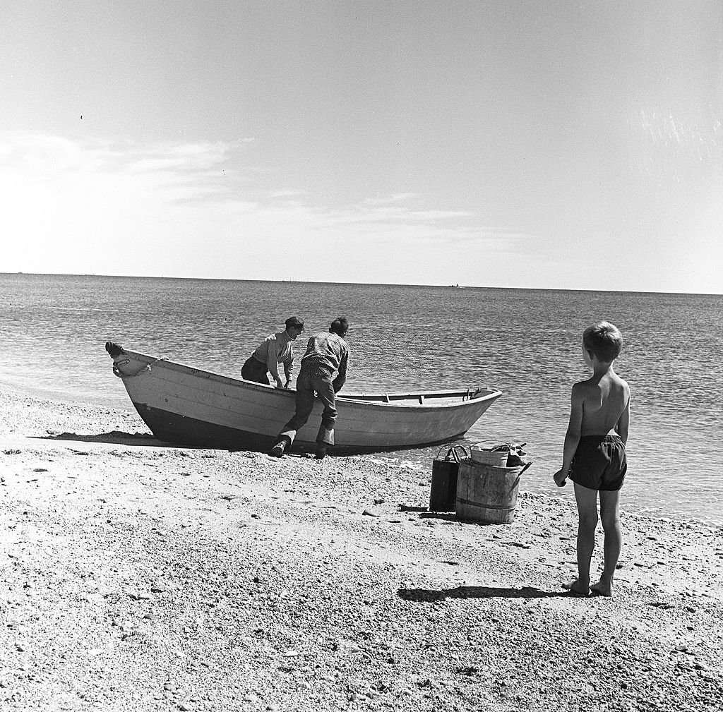 #73 A young boy watches two fishermen head out on a boat on Cape Cod, Provincetown, Massachussetts, 1947.