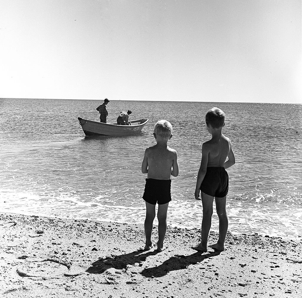 #79 Two young boys watch as two fishermen head out on a small boat on Cape Cod, Provincetown, Massachussetts, 1947.
