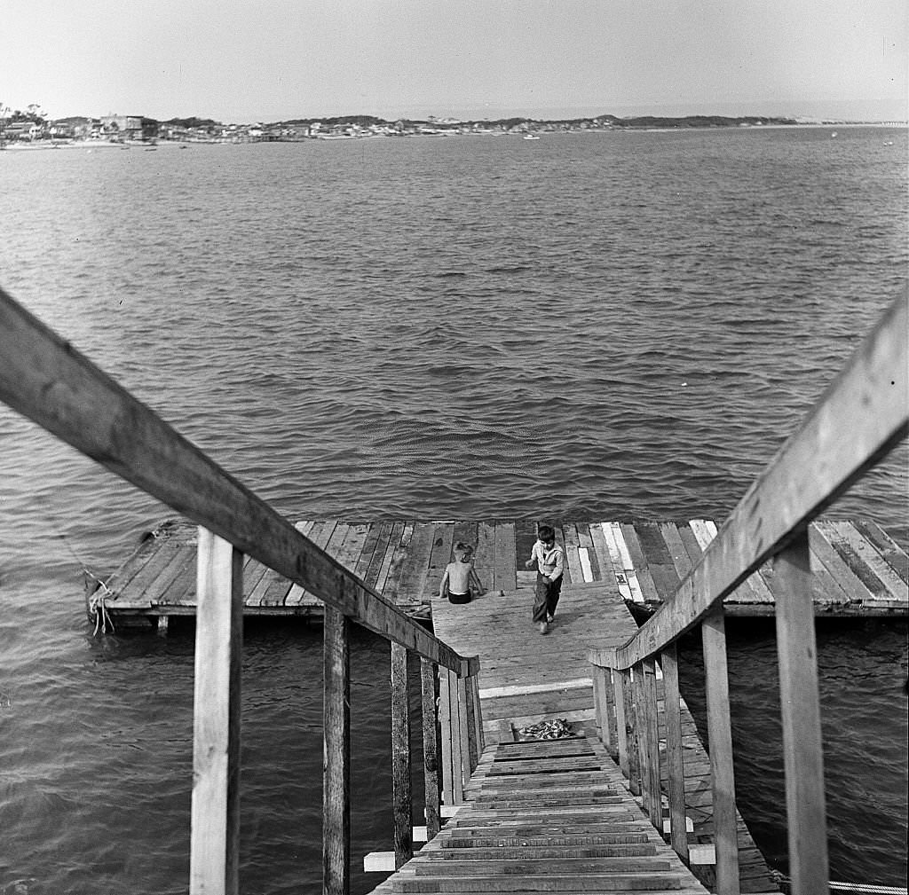 #84 View, looking down stairs, at boys playing at the end of a pier on Cape Cod, Provincetown, Massachussetts, 1947.