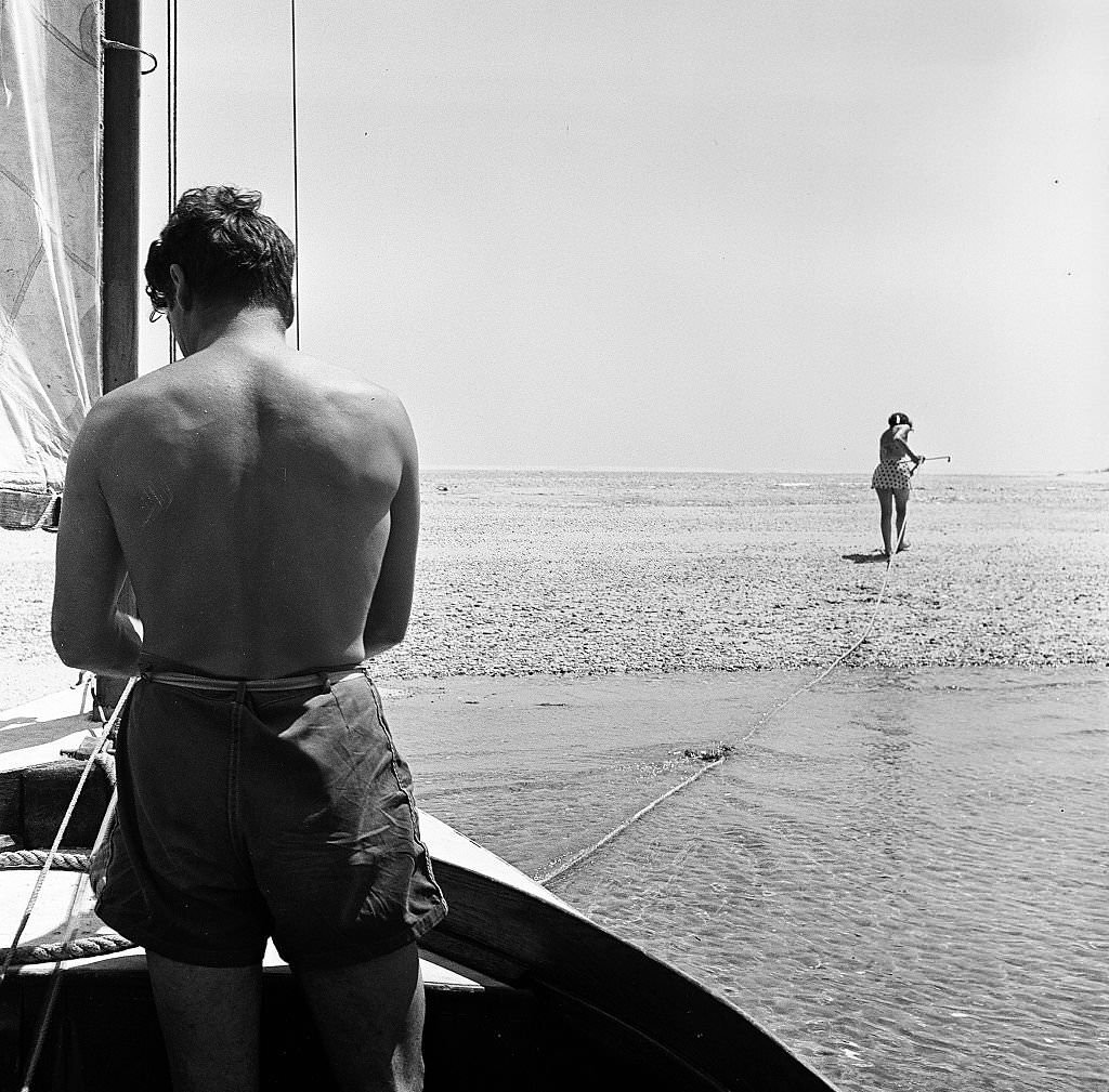 #13 A woman walks ahead to anchor the sailboat on the beach as a man waits to debark on Cape Cod, Provincetown, Massachussetts, 1947.