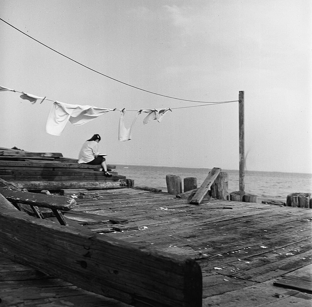 #94 acing the ocean, a girl sketches or writes in her book while sitting on the pier, Provincetown, Massachusetts, 1948.
