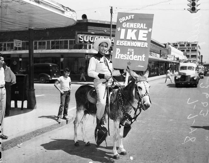 #238 Wally West in western clothing carrying sign, riding donkey, 1948