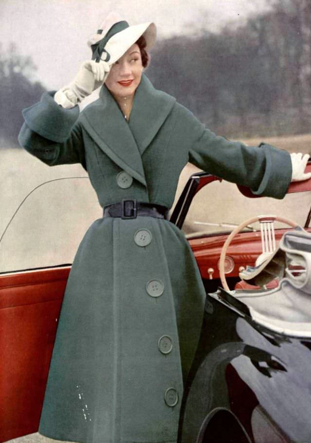 #31 Sophie Malgat in green wool coat with giant buttons lined diagonally, waist is cinched by patent leather belt, worn with white piqué hat, by Jacques Fath, 1951