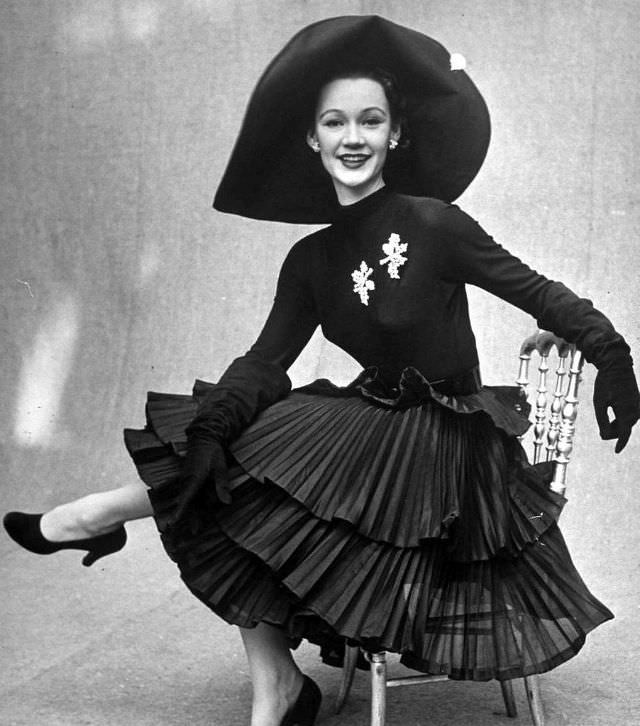 #32 Sophie Malgat in skirt featuring three tiers of pleats worn with long sleeved top and picture hat by Jacques Fath, February 1951