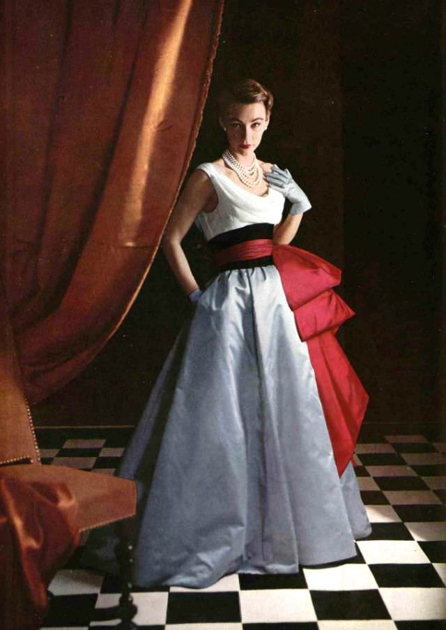 #15 Sophie Malgat in evening gown, the bodice is white chiffon with blue satin skirt and red satin sash over wide black satin waist band, by Jacques Fath, 1952