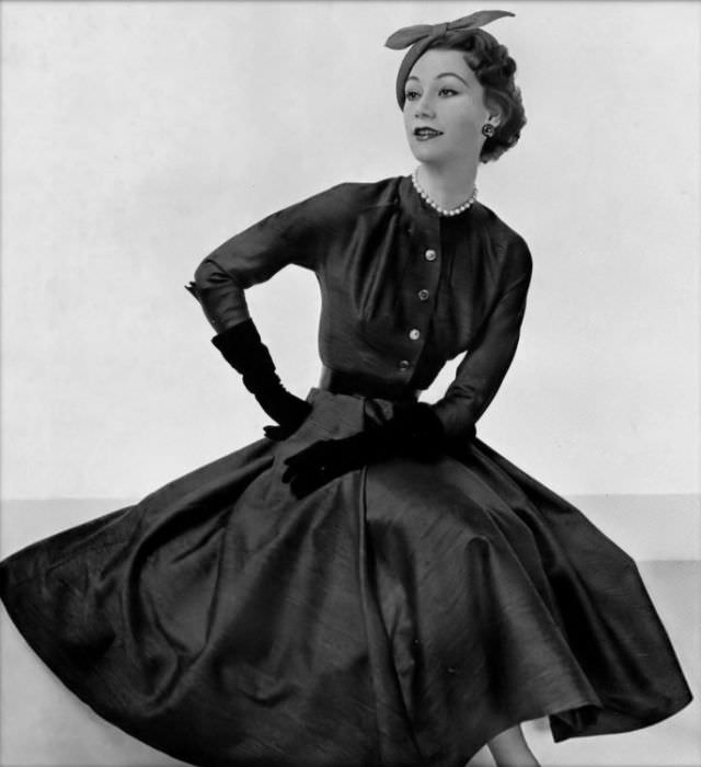#22 Sophie Malgat is wearing a dark gray alpaca wool dress with ample skirt, buttoned bodice is ruched around the neckline, by Pierre Clarence, 1953