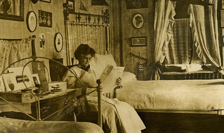 #13 Young girl student reading a newspaper in her room at Georgia Burleson Hall, Baylor University, 1910