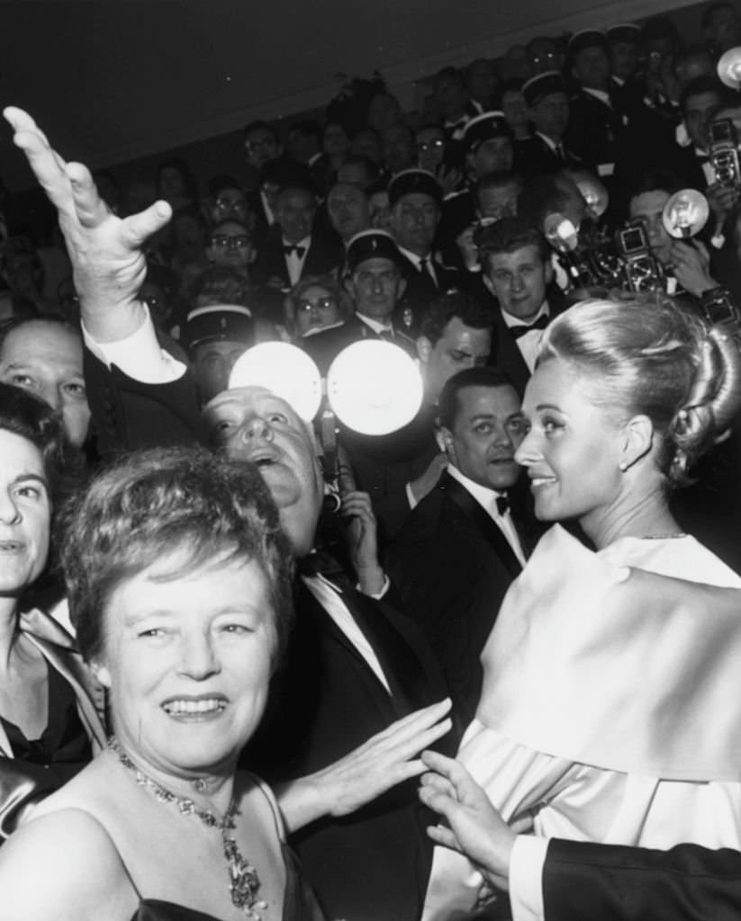 Alfred Hitchcock raising his hand in the air, with actress Tippi Hedren (right) and Mrs Hitchcock (close to camera) at the premiere of the film ‘The Birds’ at Cannes, May 11th 1963.