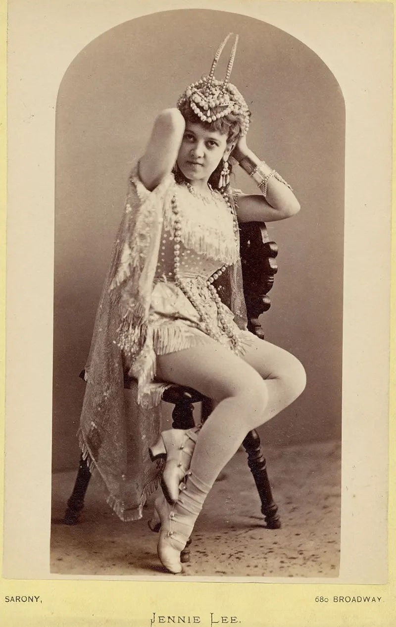 #13 Jennie Lee sitting on a chair holding a headdress.