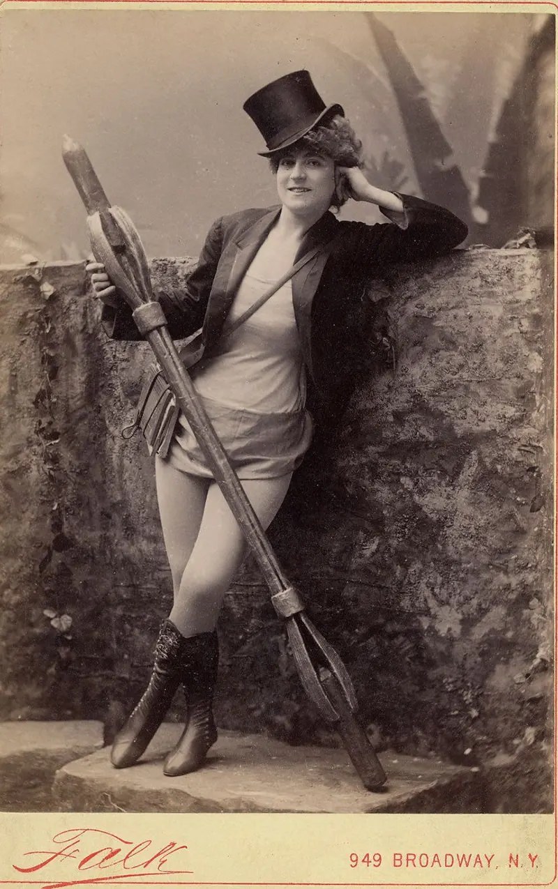 #18 Vernona Jabeau, in high boots, hat, holding a candle in a long holder.