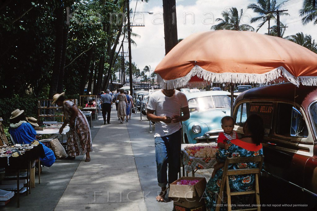 #71 Local vendors selling fresh lei and souvenirs along the makai side of Waikiki’s Kalakaua Avenue in front of the Royal Hawaiian Hotel, 1958