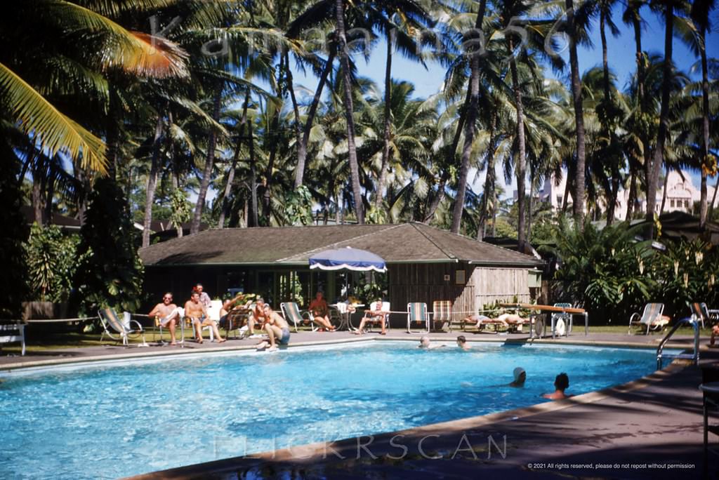 #168 Looking east across the pool deck at the Edgewater Hotel towards the Royal Hawaiian Hotel which can be glimpsed through the palm trees in the background, 1952