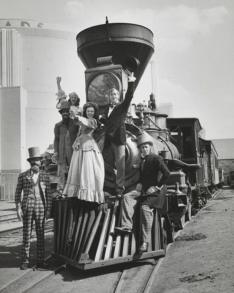 #124 View showing a group of actors in various costumes posed on the front of a steam engine.