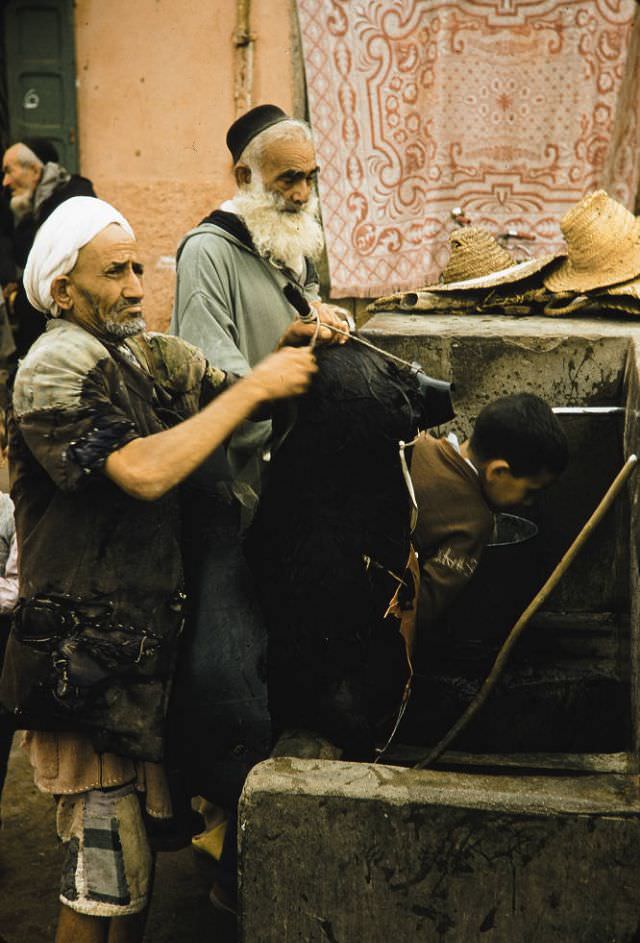 #115 Man filling animal skin with water front fountain in Marrakech, 1960s