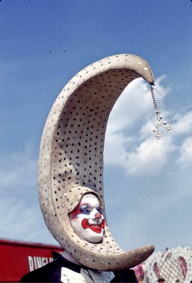 #16 A clown with a large crescent head piece in Holidays spec wardrobe.