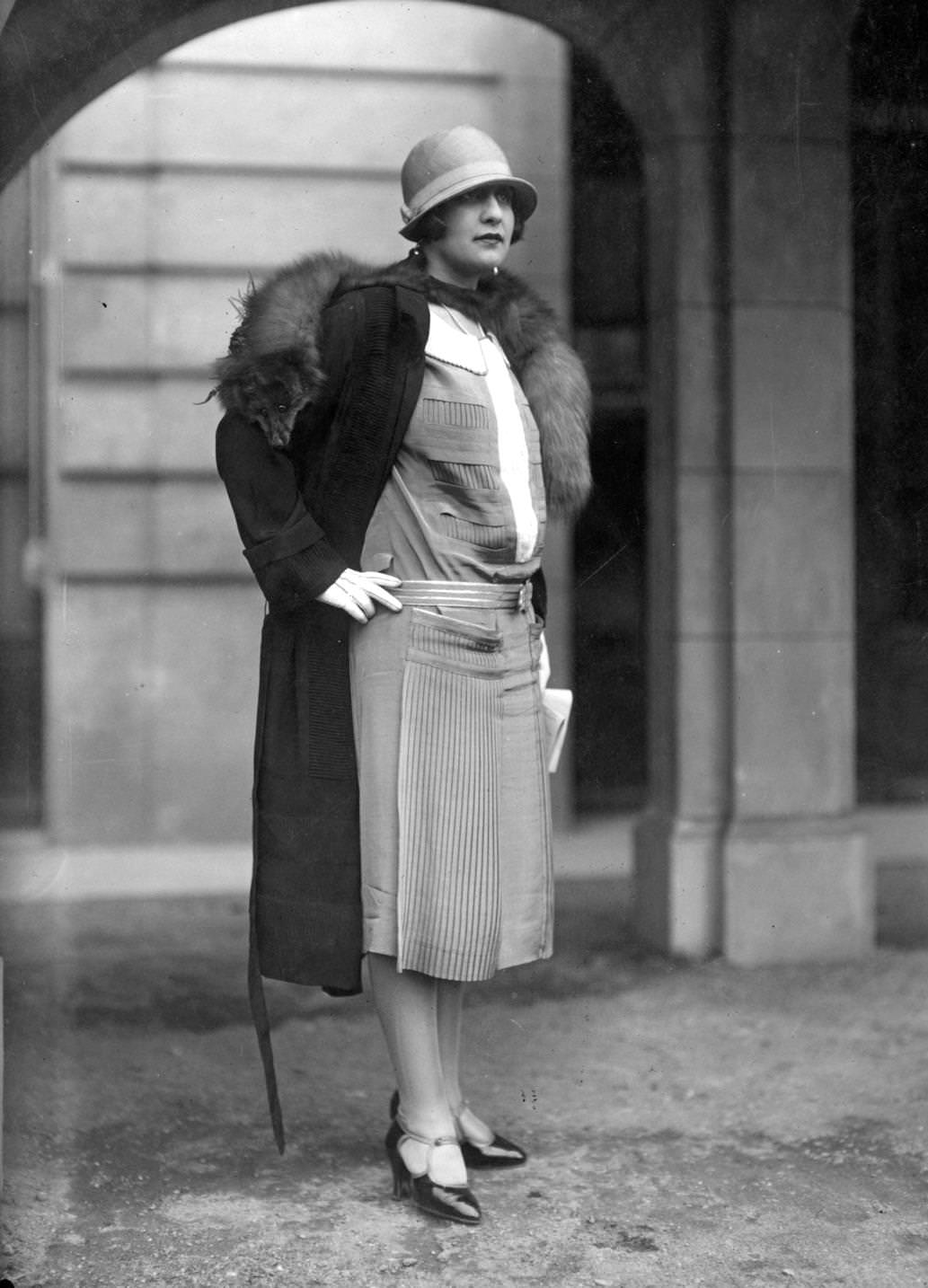 #112 Dress with pleated panels worn with a coat and fox fur and a small brimmed cloche-hat, 1925.