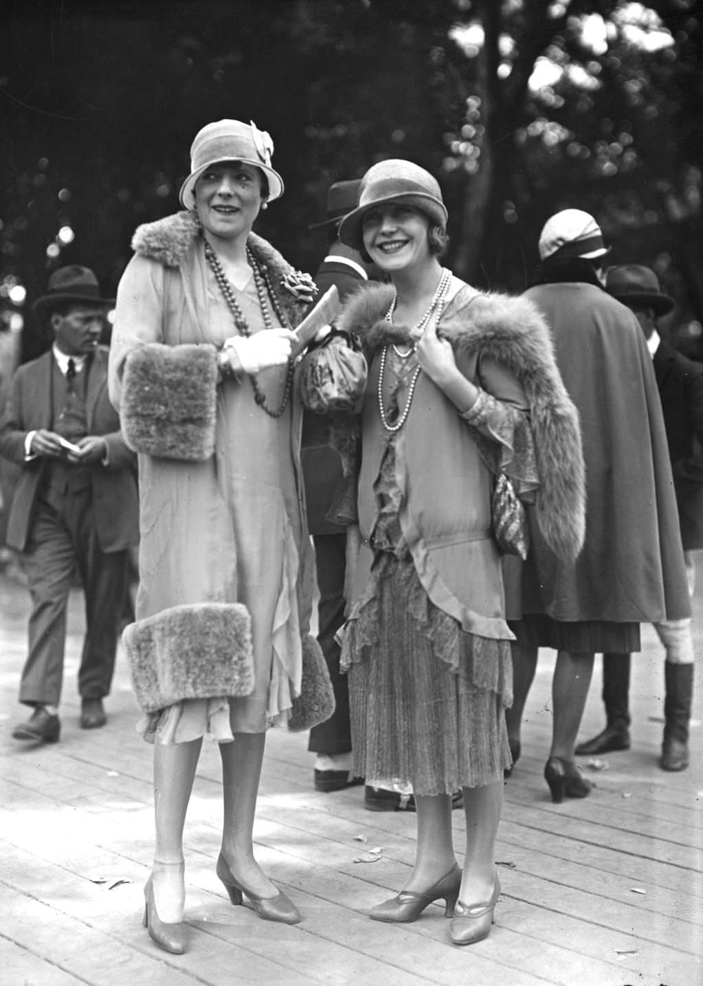 #119 Two outfits designed by Jenny. One is a light coat with wide fur trim at hem cuffs and collar worn with a cloche hat with a small brim, a double rope of beads and an anklet chain, 1925
