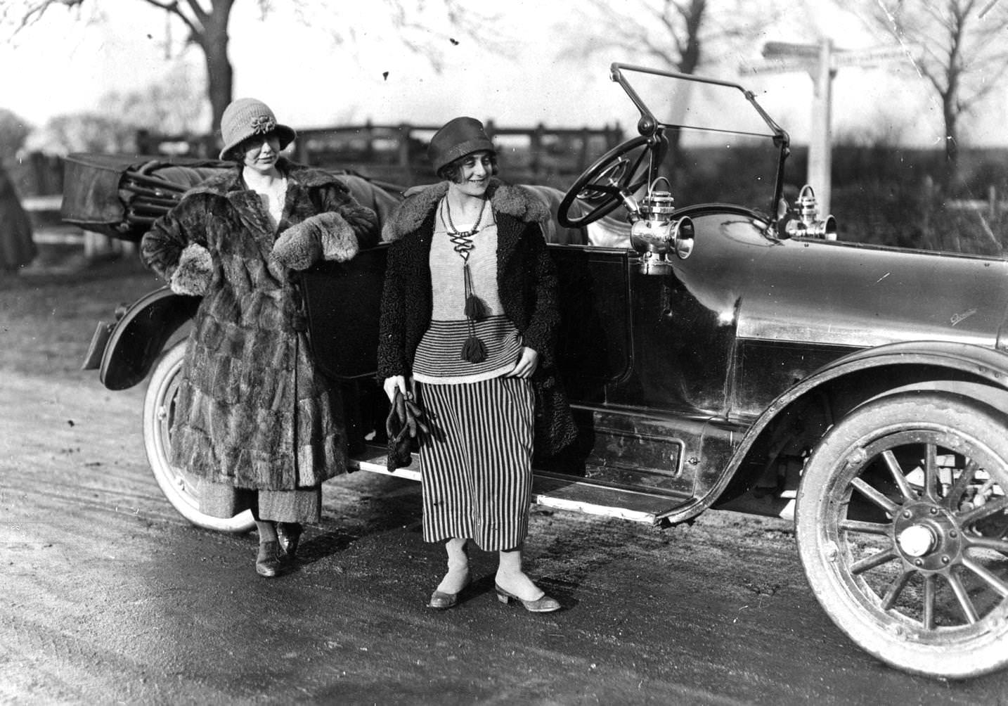 #16 Two ladies, wearing fur coats and Cloche Hat, on their way to a hunting meet, standing by their convertible car.