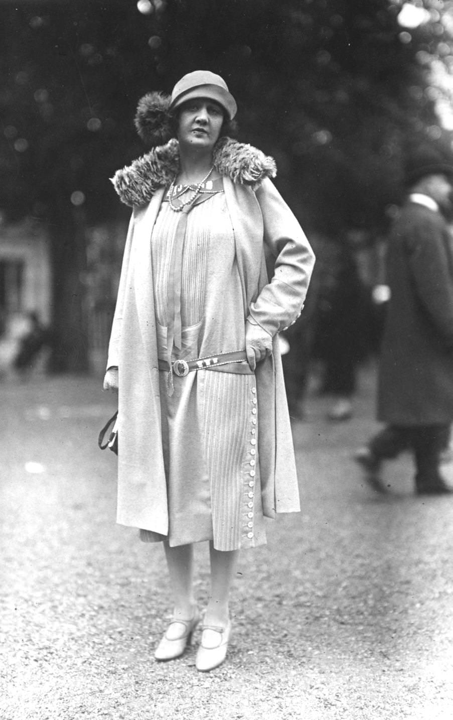 #177 Low waisted calf length dress with buttoning side panels along one side. Coat with fur collar, and cloche hat with fur pom-pom, 1925