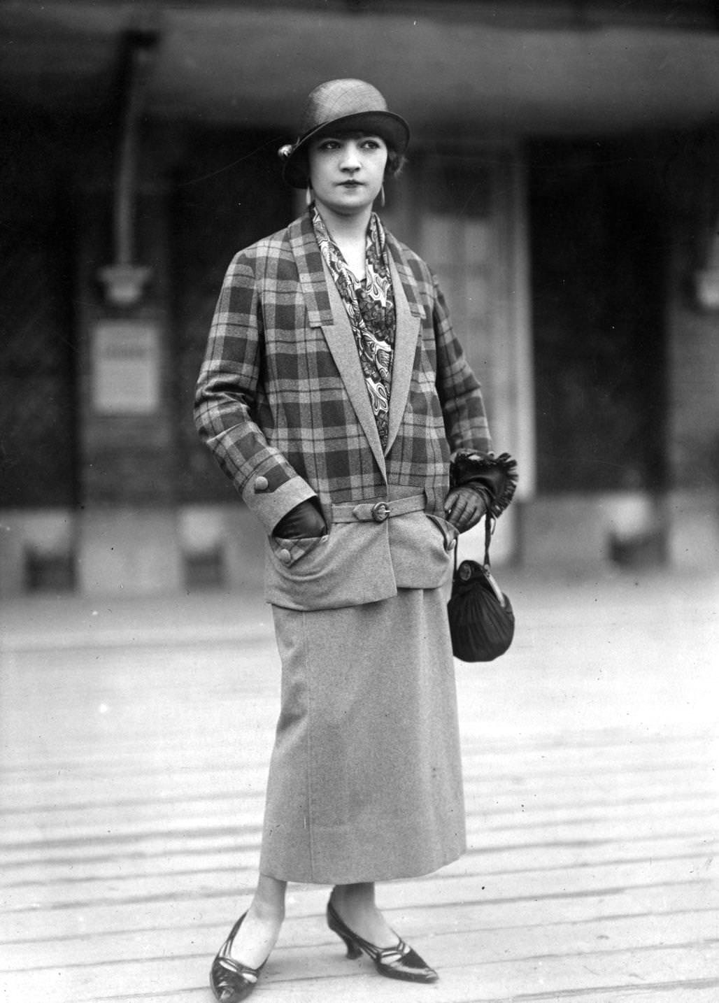 #47 V-necked suit by Felix Dupouy. Check jacket has dropped waist worn over a plain skirt. Hat is a small brimmed cloche, small pouch shaped handbag is carried over the wrist, 1924