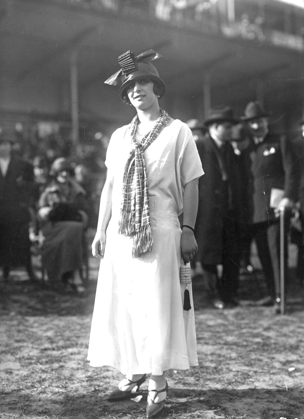 #60 Simple, loose waisted short-sleeved dress worn with a loosely knotted scarf. A hat is cloche shaped with a large bow on the front, 1924