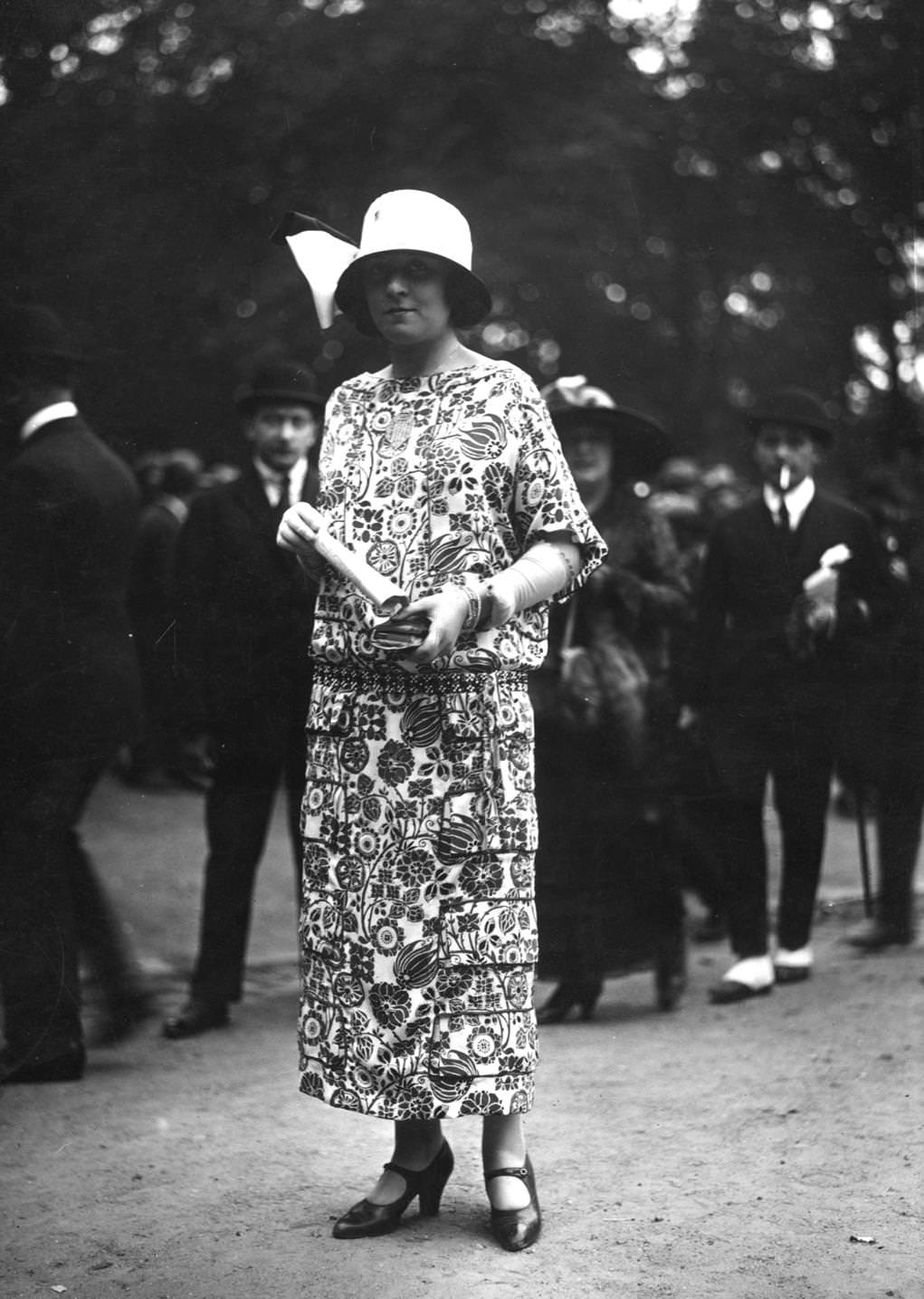 #75 Drop-waisted ankle length dress in multi-patterned material with three-quarter sleeves and elbow length gloves. Worn with a cloche hat decorated with a bow. One-bar shoes, 1923