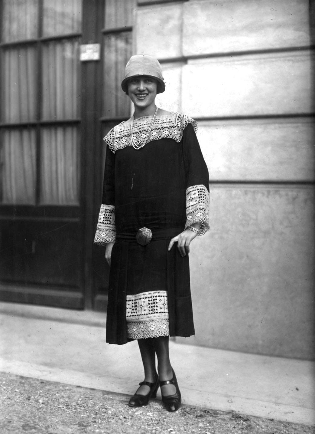 #92 Long waisted dress with lace inserts at hem and neck and as cuffs on long loose sleeves. A cloche hat, one-bar shoes and a double string of pearls completes an outfit designed by Callot, 1925