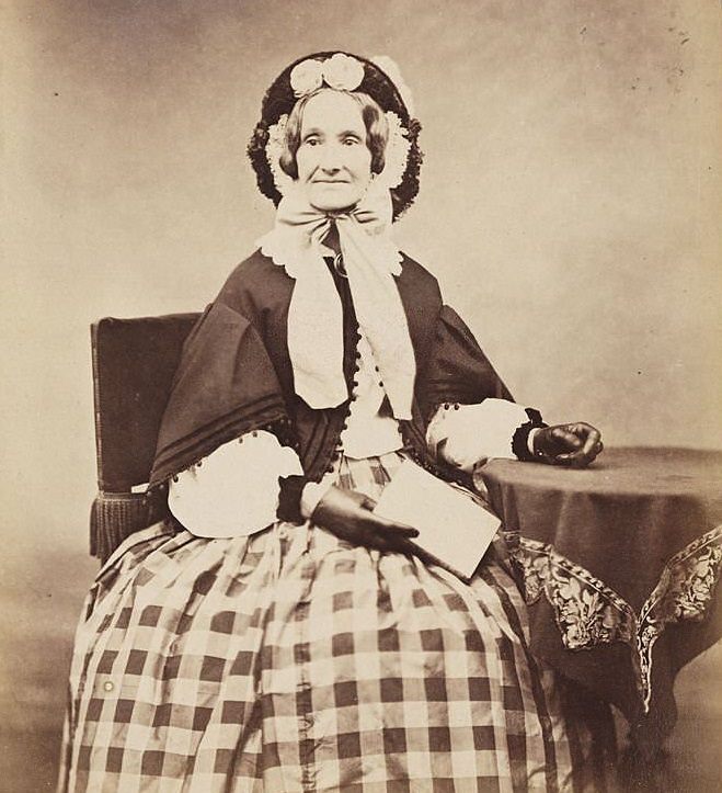#36 Victorian woman in a bonnet and checked skirt, with a book in one hand, 1860