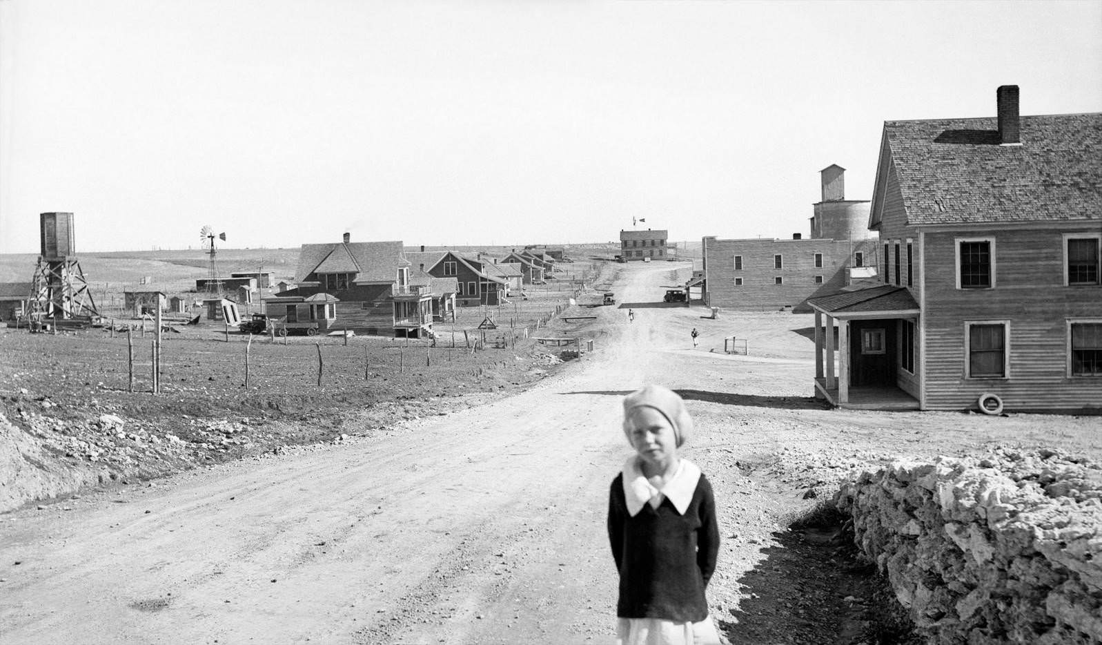 #48 Portrait of Young Girl, Street Scene with Abandoned Grain Mill and Bank both right in Background, Mills, New Mexico, 1930s