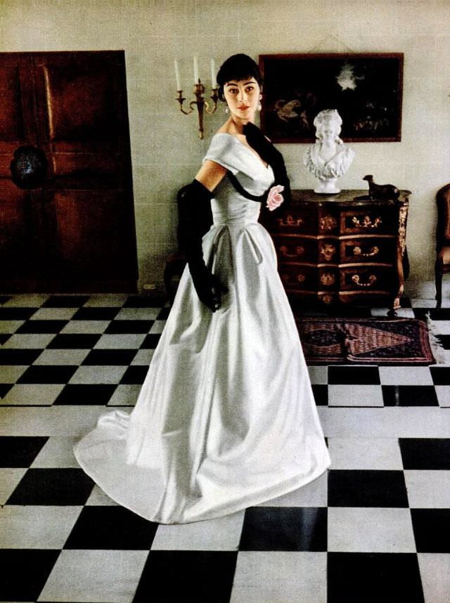 #22 Anne Gunning in white satin gown with velvet ribbon outlining the bosom by Jacques Fath, photographed in the foyer at Fath’s chateau at Corbeville by Mark Shaw, 1953