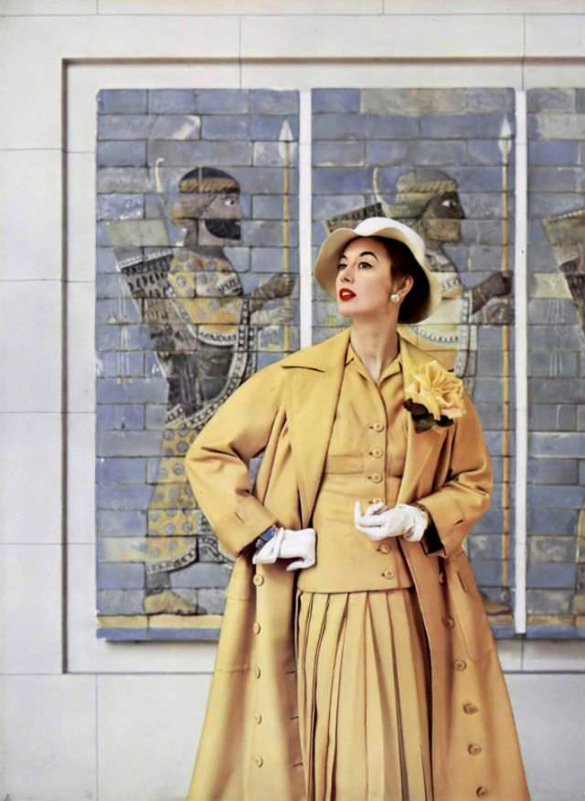 #32 Elinor in classic overcoat buttoned all the way with large patch pockets, worn over tailored suit with pleated skirt by Jacques Fath, 1954