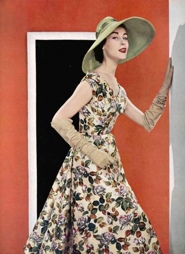 #37 Myrtle Crawford in a silk floral print afternoon dress worn with wide-brimmed green straw hat, by Jacques Fath, 1954