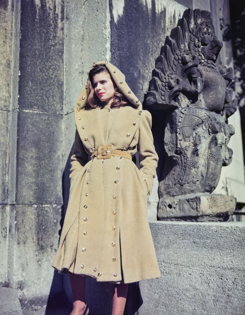 #50 A female fashion model wears a camel wool coat in beige with leather belt and gilt buttons, part of the new collection from French couture designer Jacques Fath in Paris, France, 25th October 1945.
