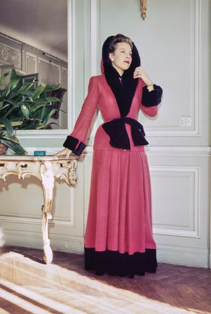 #51 A female fashion model wears a home gown of Angora jersey in red with matching hood, both trimmed with black rabbit, part of the new collection from French couture designer Jacques Fath in Paris, France, 25th October 1945.