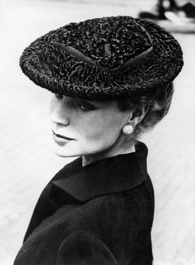#60 Round hat in gray astrakhan from South Africa. The encrusted grosgrain forms the crown. This model is worn forward on the forehead. Created by Jacques Fath, Paris 1955.