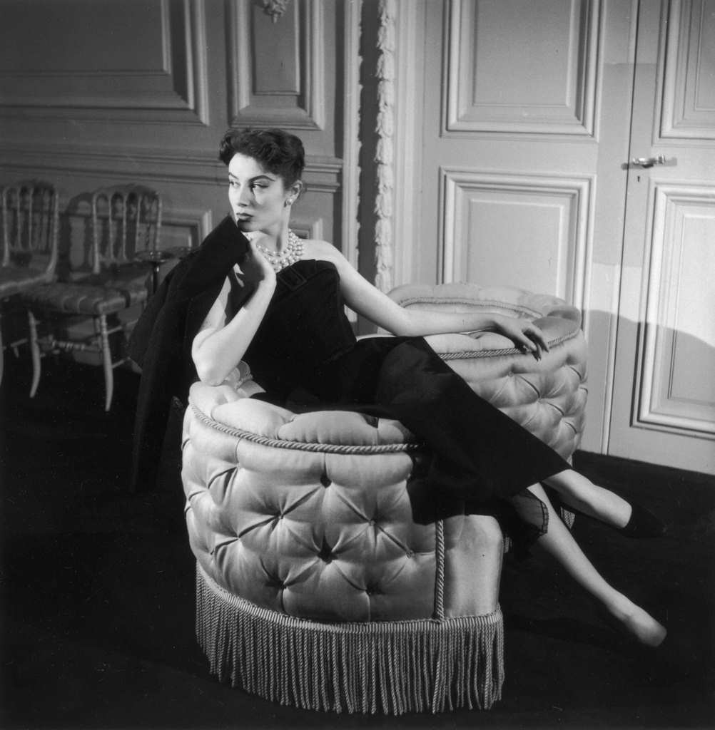 #72 Genevieve Fath lounges in a loveseat, wearing an outfit designed by her late husband, Jacques Fath, 1955