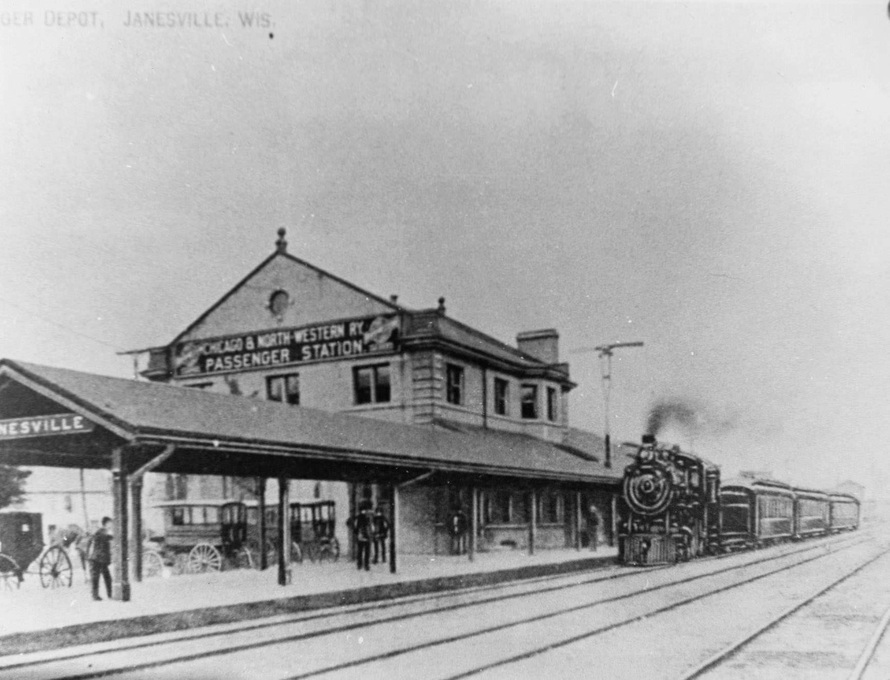 #87 The Chicago and North Western Railroad depot in Janesville with a steam locomotive on the track, 1890