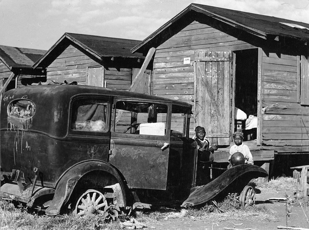 #113 Children of migratory laborers stand outside their dilapidated houses, which were condemned by the Board of Health, but still used as living spaces, Belle Glade, Florida, 1941.